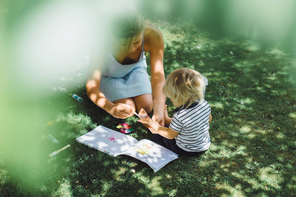 cute blonde boy with young mother on green grass outdoor - Φωτογραφία, εικόνα