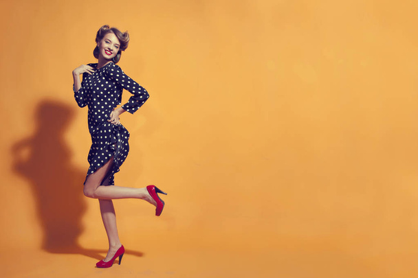 Attractive young women in polka-dot dress posing on orange background - Zdjęcie, obraz