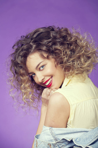 Smiling girl with curls on a lilac background - Фото, зображення