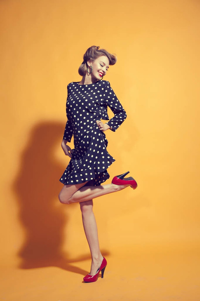 Attractive young women in polka-dot dress posing on orange background - Foto, afbeelding
