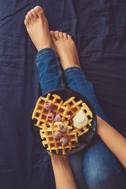 Belgian waffles with cream and frozen raspberries on blue ceramic plate in woman' s hands - Fotografie, Obrázek