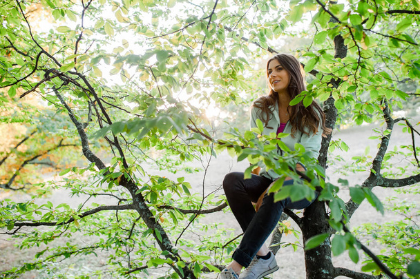 Joven mujer enérgica trepando a un árbol en el bosque, luciendo feliz, disfrutando pasar tiempo en la naturaleza tomando tiempo libre de la ciudad
. - Foto, Imagen