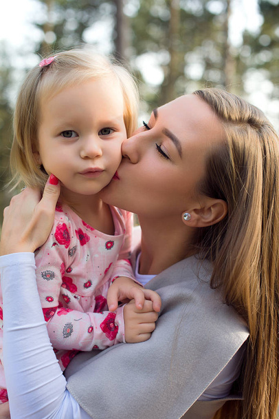 Joven madre soltera sosteniendo linda hija niña en sus brazos y dándole un beso en una mejilla
 - Foto, imagen