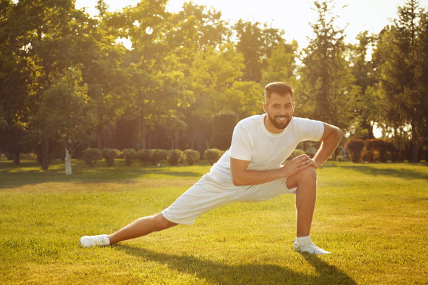 Sporty man stretching in park on sunny day - 写真・画像