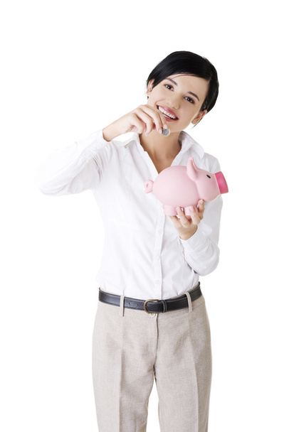 Businesswoman putting a coin into a piggy bank - Zdjęcie, obraz