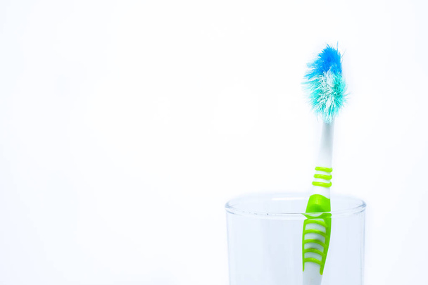 Old toothbrush (damaged) in clear glass for teeth cleaning isolated on white background - concept "How often should you change your toothbrush ? " - Photo, Image