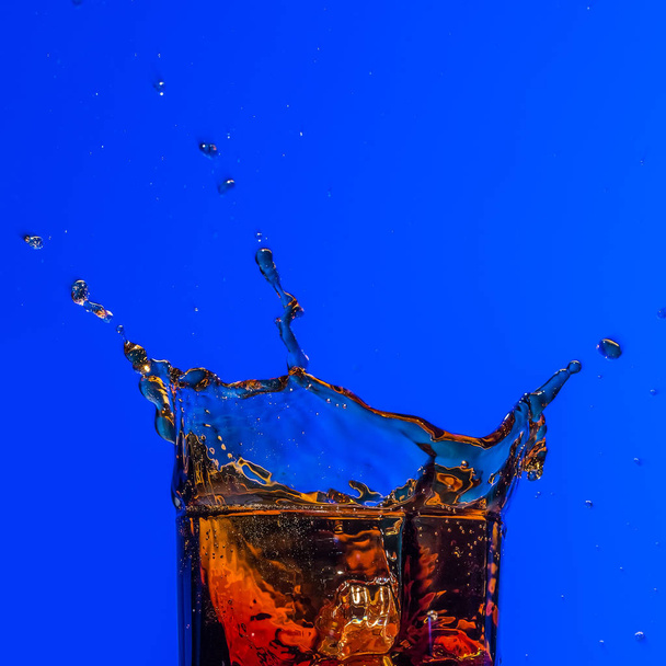 Glass with whiskey splash on blue background - Valokuva, kuva