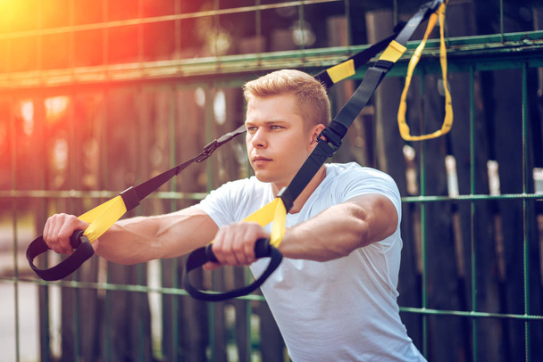 The athlete straps the muscles of chest triceps. Male athlete, engaged in hinges, close-up. Have a fence in summer. Exercise in the fresh air. The concept of a healthy lifestyle. Shine of the sun. - Foto, Imagen