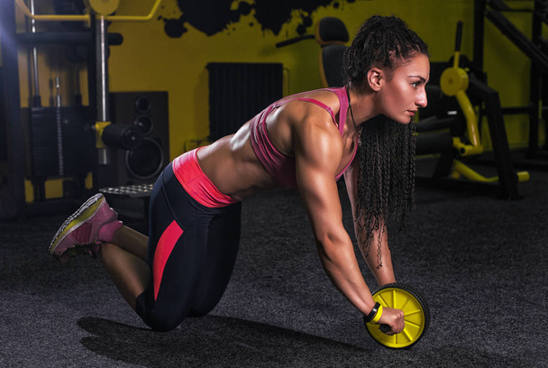 Mulher atraente exercício com rolo de roda para abdominais no chão no ginásio como parte do treinamento de fitness
 - Foto, Imagem