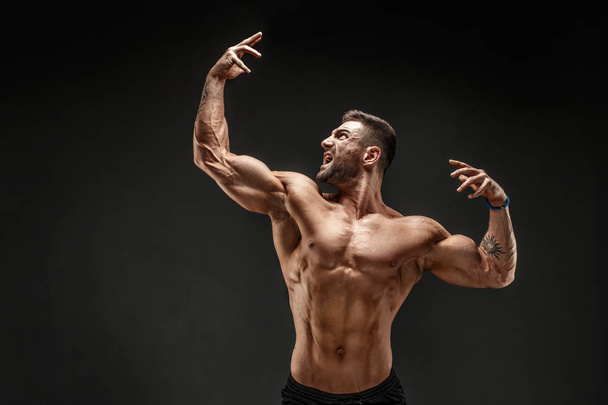 Bodybuilder posing. Fitness muscled man on dark background. - Foto, afbeelding
