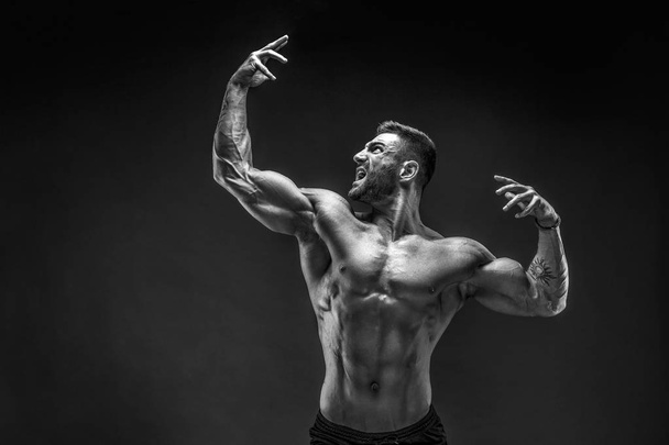 Bodybuilder posing. Fitness muscled man on dark background. - 写真・画像