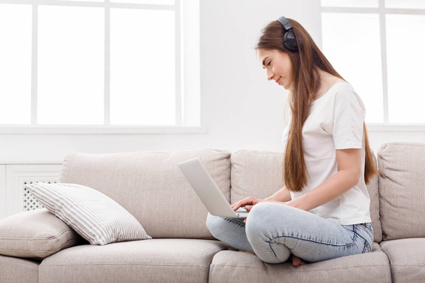 Молода жінка слухає музику і серфінг в Інтернеті на ноутбуці, копіює простір на вікні
 - Фото, зображення