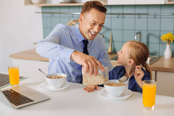 Delighted caring father adding cereal to his daughters bowl - Valokuva, kuva