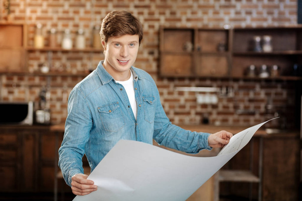 Charming young man posing with a blueprint in hands - Valokuva, kuva