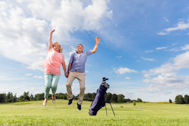 Senior couple jumping on a golf course. - Photo, image