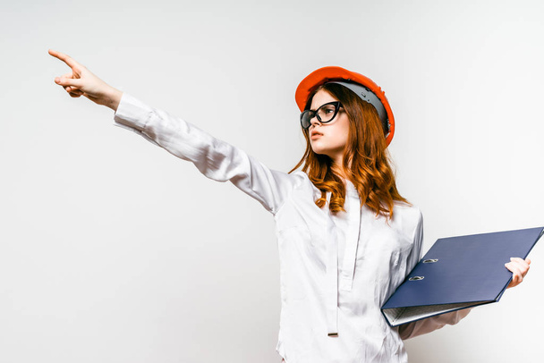 a girl in an orange construction helmet is pointing with her finger to the side - Фото, изображение