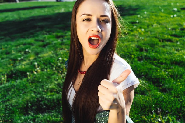 Passionate woman shows thumbs up outdoor,sit on grass - Foto, Imagem