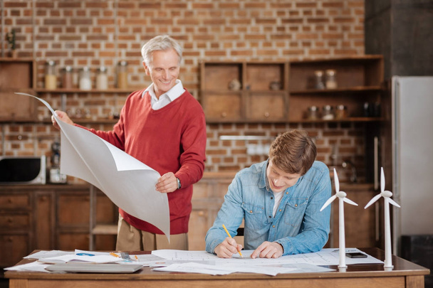 Senior man holding blueprint and watching his colleague draw one - Fotó, kép