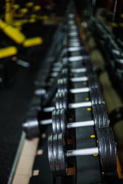 A set of dumbbells, generally used in workouts by wrestlers, bodybuilders, sports players, and others wishing to increase strength and muscle size on a dark blurred background. - Фото, зображення