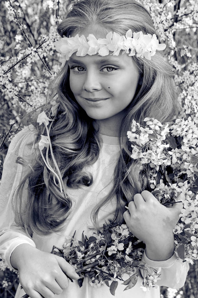 Jolie jeune fille aux longs cheveux blonds debout dans une prairie en couronne de fleurs, tenant un bouquet de fleurs de printemps et vêtue de vêtements de printemps
 - Photo, image
