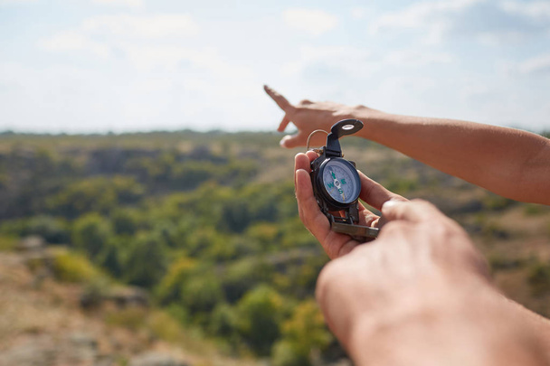 Tourists's hands with compass at mountain road at sunset sky. Close-up view of hand showing little round compass to camera, with incognito man. Point of view shot. - Foto, afbeelding
