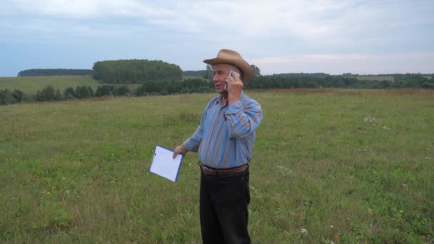 Bejaarde boer In Cowboy hoed permanent op het veld, spreekt over de telefoon - Video