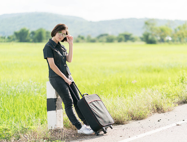 Woman with luggage hitchhiking along a road - Photo, Image