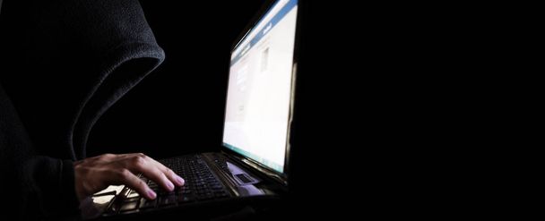Неопознанный хакер в Черной Шапочке с помощью ноутбука. Выборочный фокус, панорамный черный фон с копировальным пространством
 - Фото, изображение