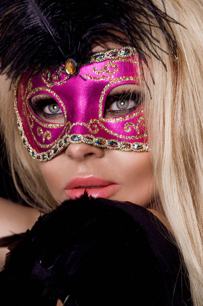 Mulher loira sensual bonita com máscara de carnaval, de pé sobre um fundo de balões pretos e sexy olha para a lente
 - Foto, Imagem