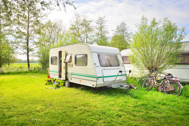 White caravan trailer on a green lawn in a camping site. Sunny day. Spring landscape. Europe. Lifestyle, travel, ecotourism, road trip, journey, vacations, recreation, transportation, RV, motorhome - Foto, Imagen