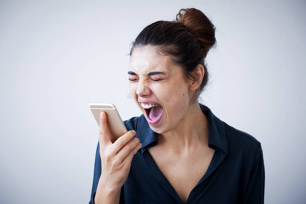 Mujer enojada gritando en el teléfono sobre fondo gris
 - Foto, imagen