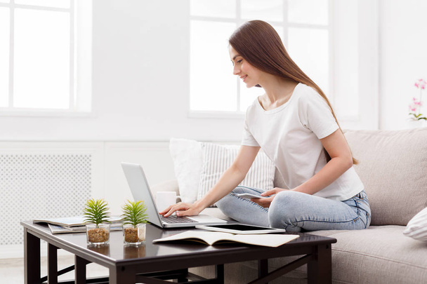 Pretty girl typing on laptop at home on the couch. Dark-haired girl in casual - Photo, Image