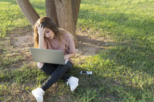 Девочка-подросток сидит на лужайке с ноутбуком
.  - Фото, изображение