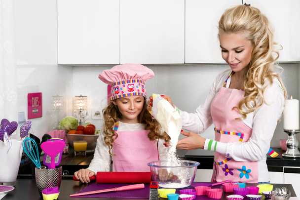 Hermosa mujer impresionante madre e hija en delantales cocina cocina en las galletas de cocina y fideos de pasta
 - Foto, imagen