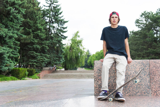 Skater se sienta con la espalda y piensa al lado del monopatín
 - Foto, imagen