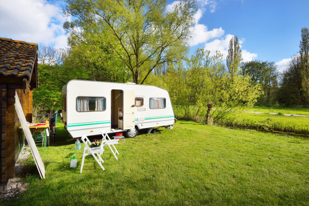 White caravan trailer on a green lawn in a camping site. Sunny day. Spring landscape. Europe. Lifestyle, travel, ecotourism, road trip, journey, vacations, recreation, transportation, RV, motorhome - Foto, immagini