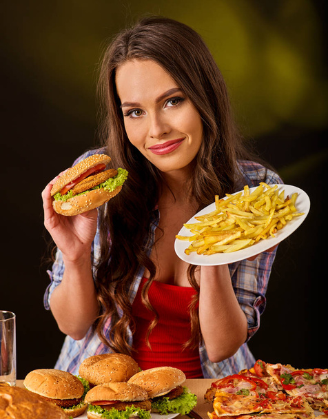 Mulher comendo batatas fritas e hambúrguer na mesa
. - Foto, Imagem