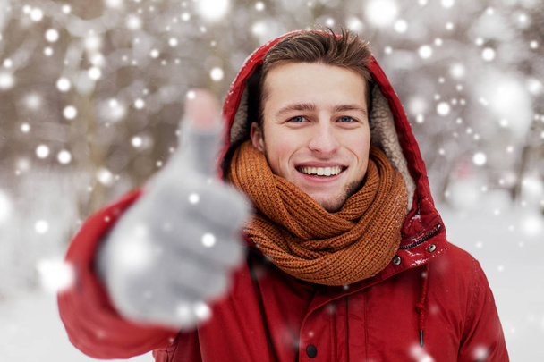 happy man in winter jacket showing thumbs up - Foto, Bild