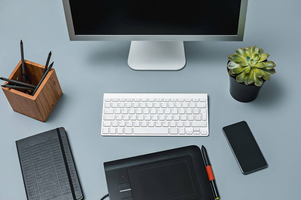 De grijze Bureau met laptop, Kladblok met blanco vel, pot met bloem, naald en tablet voor retoucheren - Foto, afbeelding