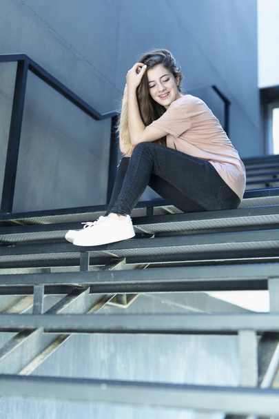 Adolescente sorrindo sentado em uma escada de metal
 - Foto, Imagem