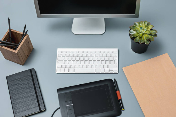 El escritorio gris con portátil, bloc de notas con hoja en blanco, maceta de flores, lápiz y tableta para retocar
 - Foto, imagen