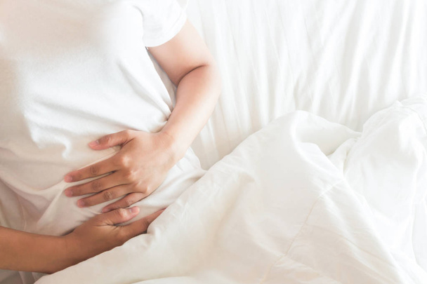 Primer plano mujer mano celebración abdominal con dolor de estómago acostado en la cama, cuidado de la salud y el concepto médico
 - Foto, Imagen
