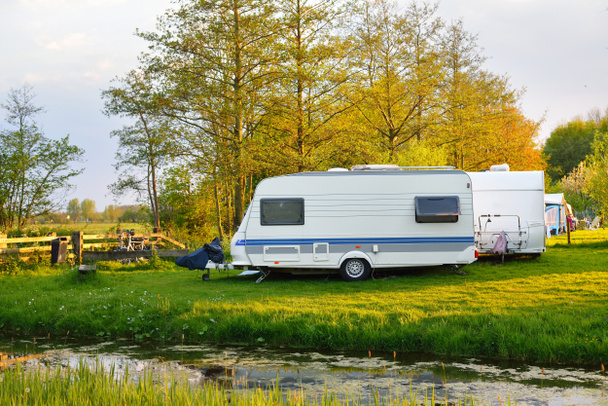 Witte caravan trailer op een groen grasveld op een camping. Zonnige dag. Voorjaarslandschap. Europa. Lifestyle, reizen, ecotoerisme, road trip, reizen, vakanties, recreatie, transport, camper, camper - Foto, afbeelding