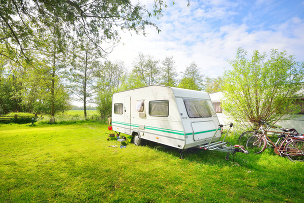 White caravan trailer on a green lawn in a camping site. Sunny day. Spring landscape. Europe. Lifestyle, travel, ecotourism, road trip, journey, vacations, recreation, transportation, RV, motorhome - Photo, Image