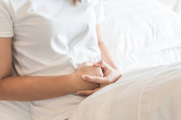 Zbliżenie kobieta ręki trzymającej brzucha z brzucha leżąc na łóżku, pojęcie opieki zdrowotnej i medycznej - Zdjęcie, obraz