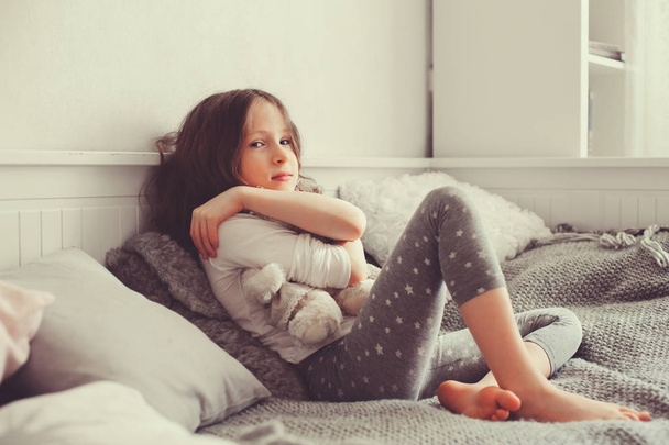 szczęśliwy dziewczyna bawi się misie w jej pokoju, siedząc na łóżku w piżamy - Zdjęcie, obraz
