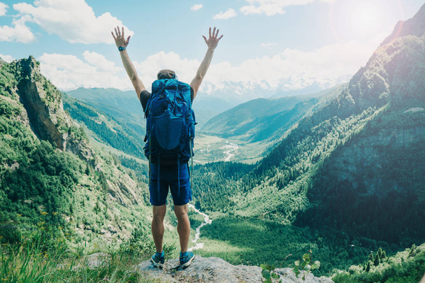 мандрівник з рюкзаком на краю скелі підняв руки в повітряних горах на задньому плані
 - Фото, зображення