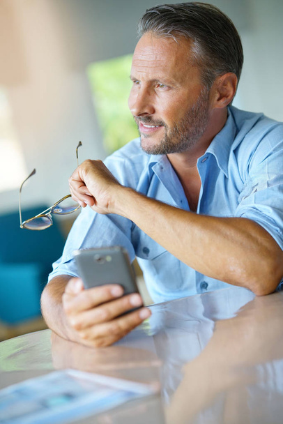 Mature man being thoughtful looking at message on smartphone  - Foto, Imagen