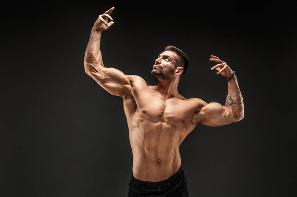 Bodybuilder posing. Fitness muscled man on dark background. - Фото, изображение