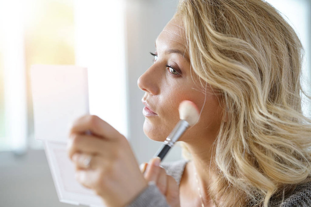 blond woman putting makeup on - Foto, afbeelding